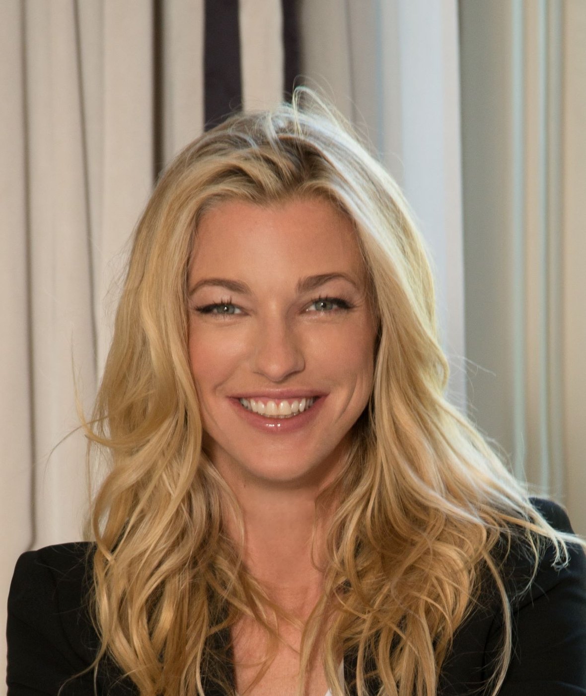 Nicole Brachetti Peretti smiling in a dark blazer, a warm studio portrait